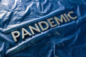 the word pandemic laid with silver letters on crumpled blue plastic film - diagonal perspective composition with selective focus photo