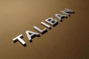 la palabra talibán colocada con letras de metal plateado sobre una tela de lona color caqui marrón áspera foto