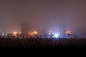 Dry dark grass field in front of foggy night depressive suburbs ghetto with photo