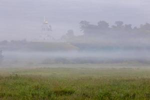 brumoso paisaje matutino de verano con la iglesia en la colina al fondo foto