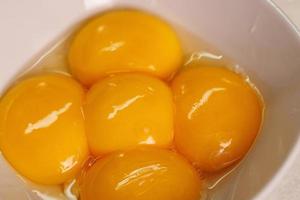 close-up view of five raw chicken egg yolks in a white ceramic bowl