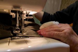 una mano de mujer anciana con un dedo vendado cose con una máquina de coser foto