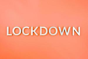 the word lockdown laid with brushed aluminium metal letters on lush lava orange color background photo