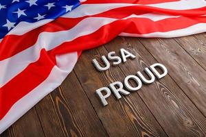 words USA proud laid with silver metal letters on brown wooden surface with flag of United States of America photo