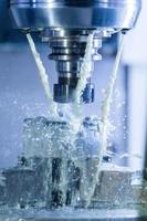 Vertical photo of industrial wet milling process in 5-axis cnc machine with coolant flow under pressure and freezed splashes