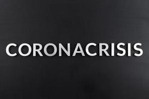 the word coronacrisis laid with white brushed metal letters on flat black surface photo