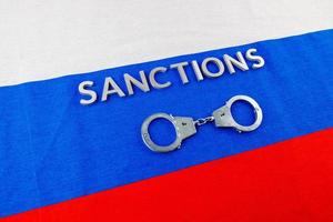 the word sanctions laid with silver metal letters on russian tricolor flag near handcuffs in directly above view photo