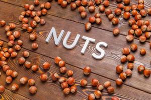 the word nuts laid with silver letters on wooden board background surrounded with scattered hazelnuts photo