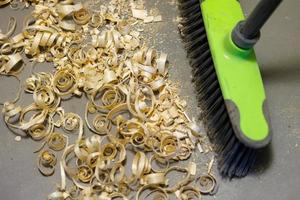 a small pile of wood shavings on a gray linoleum floor with a broom brush photo
