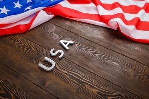 the word USA laid with silver metal letters on wooden board surface under crumpled flag of United States of America photo