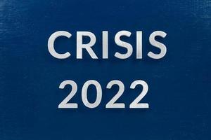 the words crisis 2022 laid with aluminium letters on blue painted board photo