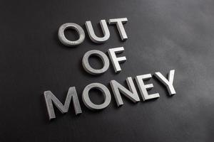 the words out of money laid with white brushed metal letters on flat black surface with diagonal composition and selective focus photo
