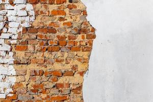 old bad brick wall with leftovers of white peeled thick plaster photo