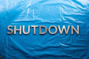 the word shutdown laid with silver metal letters on crumpled blue plastic film background in flat lay perspective photo