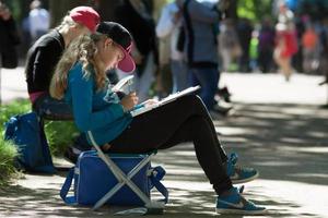 SAINT-PETERSBURG, RUSSIA, JUNE, 11 2014, Pretty blonde teen drawing plain air work in shade of sunny park. photo