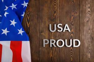 words USA proud laid with silver metal letters on brown wooden surface with flag of United States of America photo