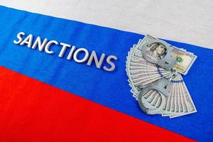 the word sanctions laid with silver metal letters on russian tricolor flag near dollar banknotes and handcuffs in diagonal perspective photo