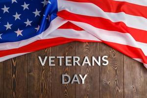 the words veterans day laid with silver metal letters on wooden board surface with crumpled usa flag photo