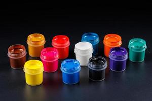 close-up background of opened small gouache paint jars on black surface photo