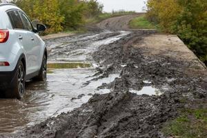 clean white suv car moving on dirt road with wet clay in front of blurry slope photo