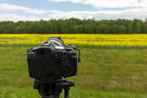 cámara sin espejo profesional moderna en trípode disparando campo amarillo en trípode, primer plano foto