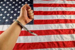 caucasian hand cuffed with silver metal handcuffs over US flag background photo