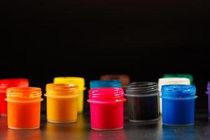 close-up background of opened small gouache paint jars on black surface photo