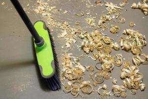 a small pile of wood shavings on a gray linoleum floor with a broom brush photo