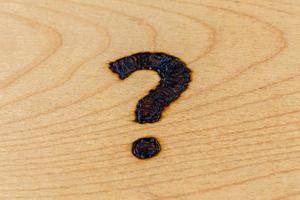 question mark drawn with handheld woodburner on bright flat wooden surface with selective focus photo