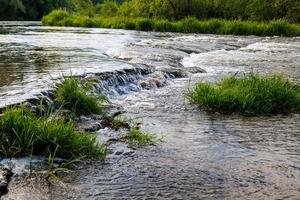 agua que fluye de un río de verano con una pequeña cascada rápida y pequeñas islas de hierba a la luz del día foto