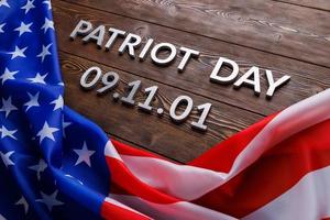 the words patriot day laid with silver metal letters on wooden board surface with crumpled usa flag photo
