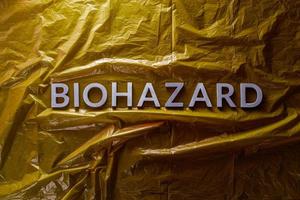 the word biohazard laid with silver letters on yellow crumpled plastic film background in flat lay composition at center photo