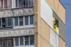 tula, rusia 10 de octubre de 2020 trabajador escalador industrial que aplica aislamiento adicional de espuma de poliestireno en la pared exterior de un edificio de apartamentos de nueve pisos foto