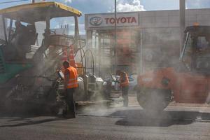 tula, rusia 16 de mayo de 2021 proceso de asfaltado, máquina pavimentadora de asfalto y apisonadora durante las obras de construcción de carreteras, en el día de verano foto