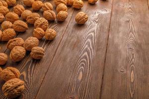many walnuts with shells randomly scattered on brown wooden surface with copy space at right side of picture photo