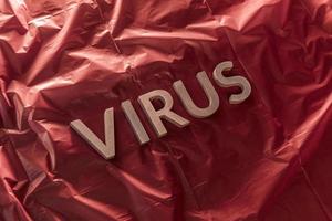 the word virus laid with silver metal letters on crumpled red plastic film with dramatic light photo