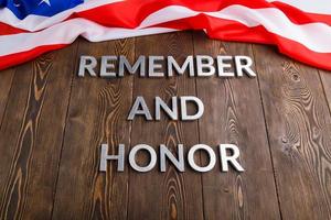 las palabras recuerdan y honran colocadas con letras de metal plateado sobre fondo de madera con la bandera de EE.UU. en el otro lado foto