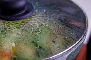 vegetables in frying pan covered with glass lid with water condensation drops on inner surface photo