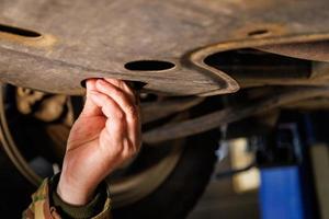 bare caucasian hand unscrews the drain plug of the engine crankcase to change the oil photo