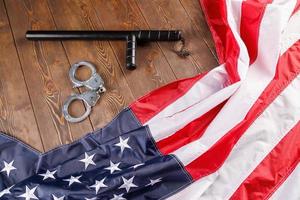 silver metal handcuffs and police nightstick near US flag on wooden surface photo