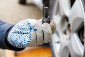 mechanic hand in fabric glove holding car wheel bolt photo