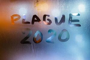 las palabras plaga 2020 escritas a mano en la superficie de vidrio de la ventana de sudor por la noche foto