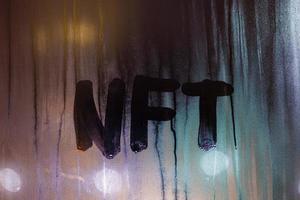 the word NFT - non-fungible token handwritten on foggy window glass at night photo