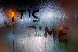 the words it's time written on night wet window glass close-up with blurred lights background photo