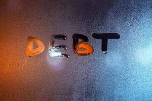 the word debt written on night wet window glass close-up with blurred background photo