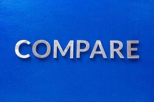 the word compare laid with silver metal characters on blue painted wooden board in flat lay with central composition photo