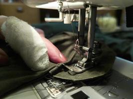 a hand of aged womans with a bandaged finger sews with a sewing machine photo