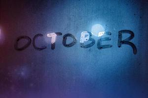 la palabra octubre escrita a mano en la superficie de vidrio de la ventana mojada de noche foto
