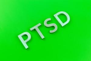 abreviatura ptsd - trastorno de estrés postraumático - colocado con letras de metal plateado sobre una superficie plana de color verde ácido foto