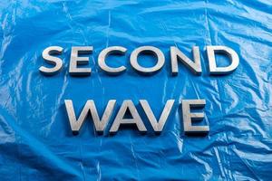 the words second wave laid with silver metal letters over crumpled blue plastic film background in linear perspective photo